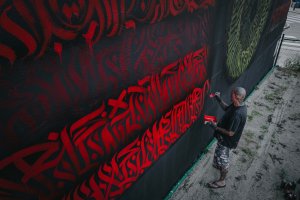 L'artiste REID entrain de peindre LE MUR utilisant de la couleur rouge.