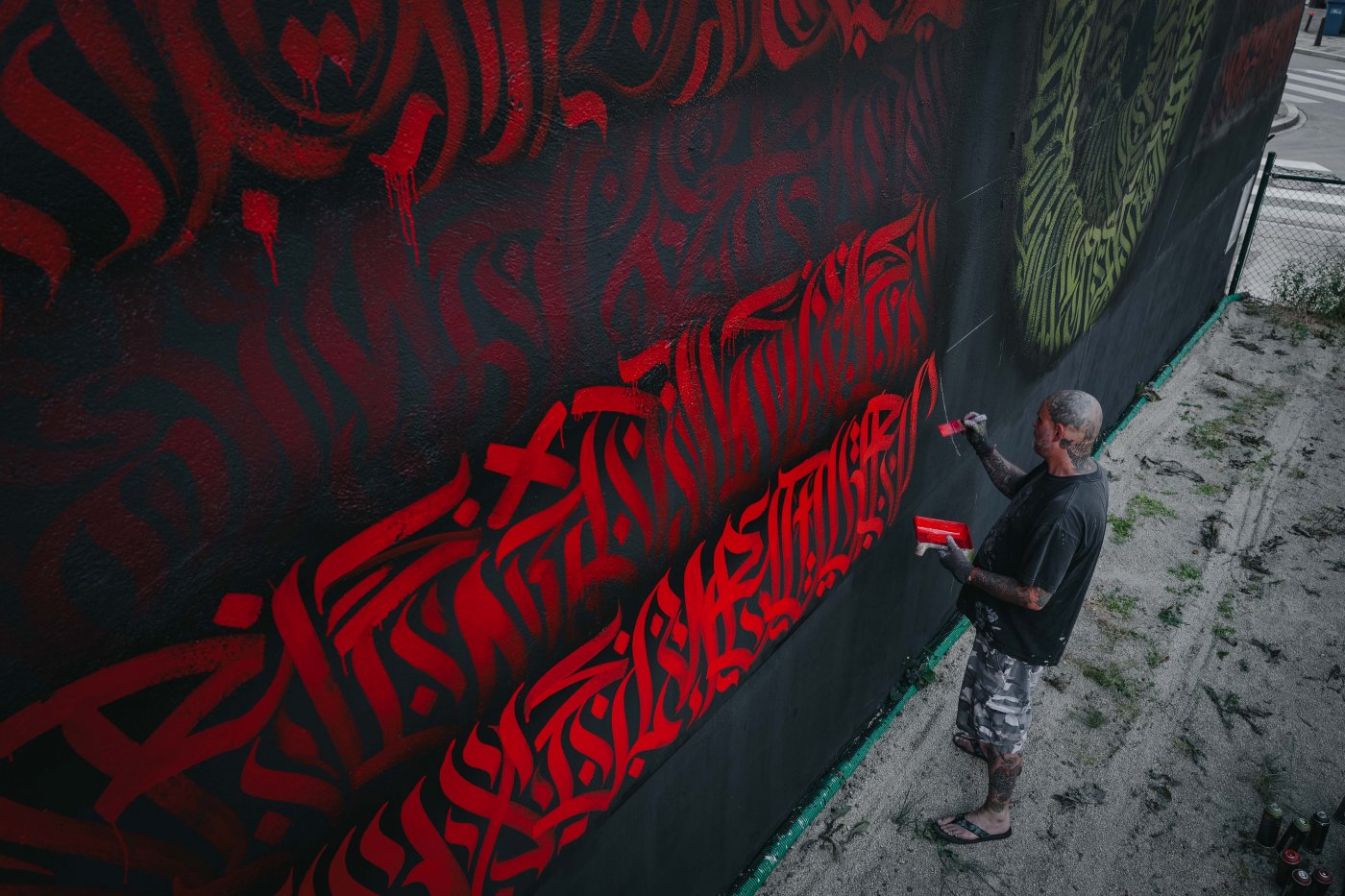 L'artiste REID entrain de peindre LE MUR utilisant de la couleur rouge.